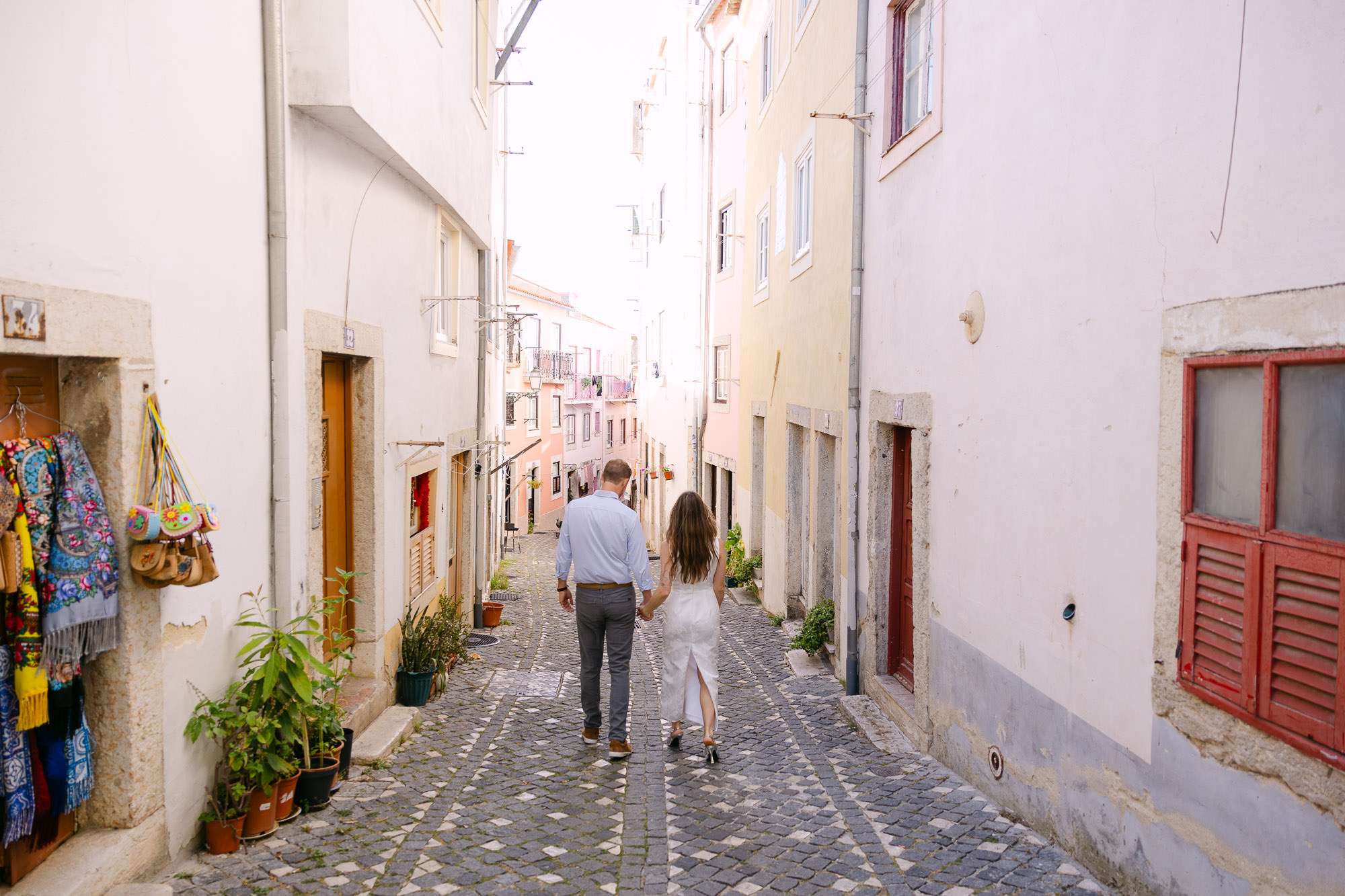 Engaged couple walking hand in hand through narrow Alfama street Lisbon, documentary save the date photography Portugal