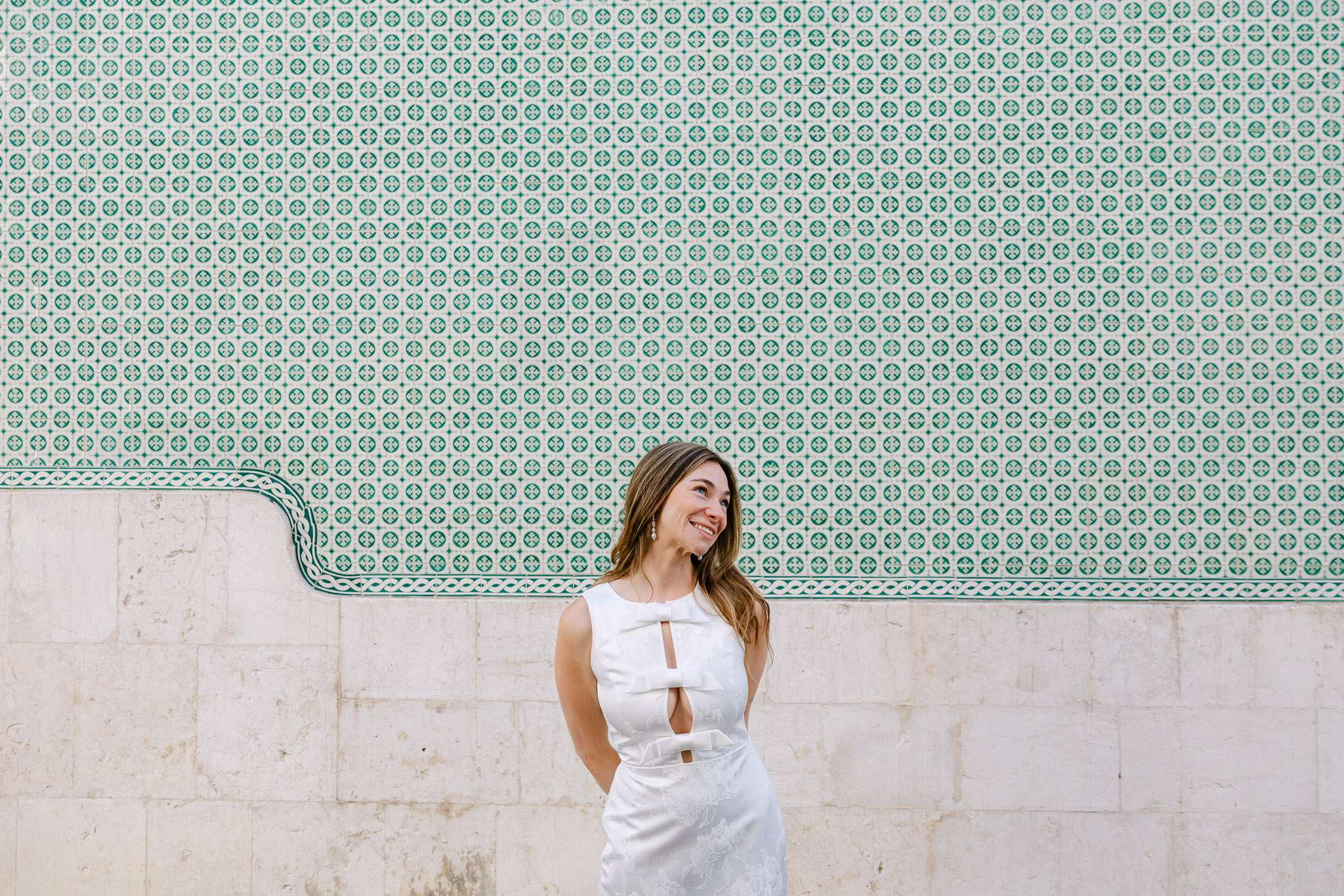 Woman in white dress smiling against green azulejo tile wall in Lisbon, couples session portrait photography Portugal