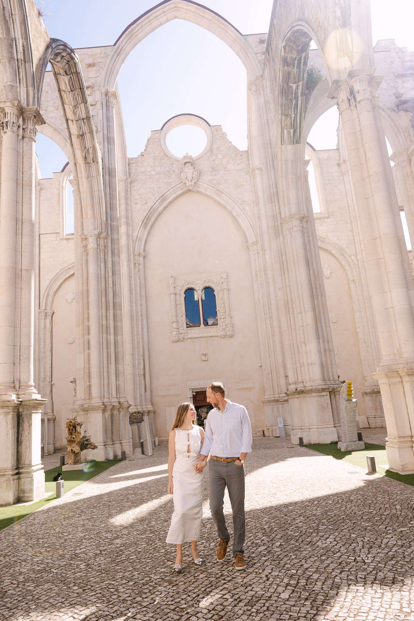 Engaged couple walking through roofless Convento do Carmo church Lisbon, smiling at each other, couples session photography