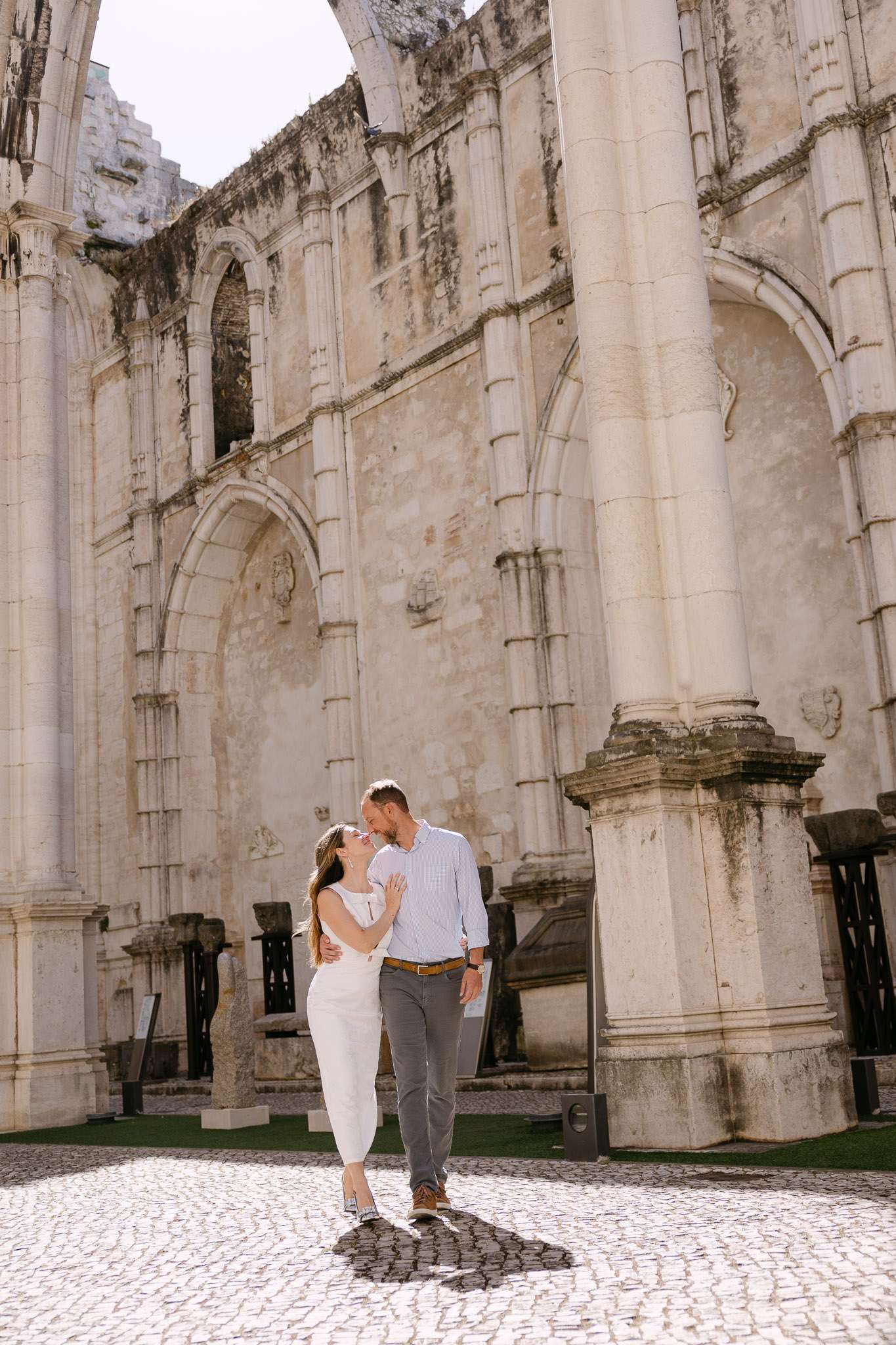 Couple kissing inside Convento do Carmo ruins Lisbon, Gothic stone arches overhead, documentary engagement photography Portugal