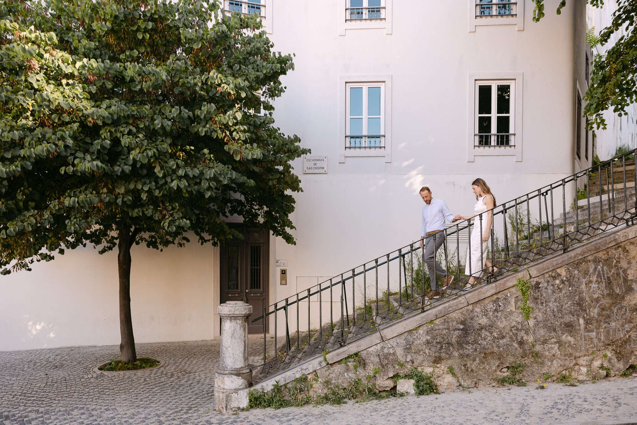 Couple descending Escadinhas de São Crispim stone steps in Alfama Lisbon, engagement photography Portugal