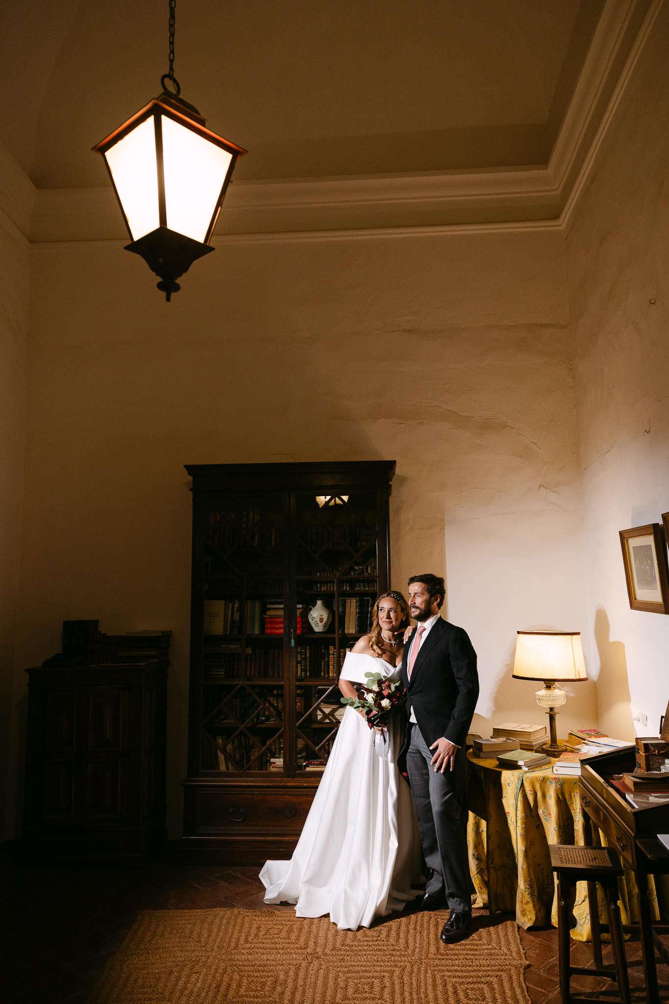 Bride and groom in candlelit manor library, antique bookcase and hanging lantern, destination wedding photographer Portugal