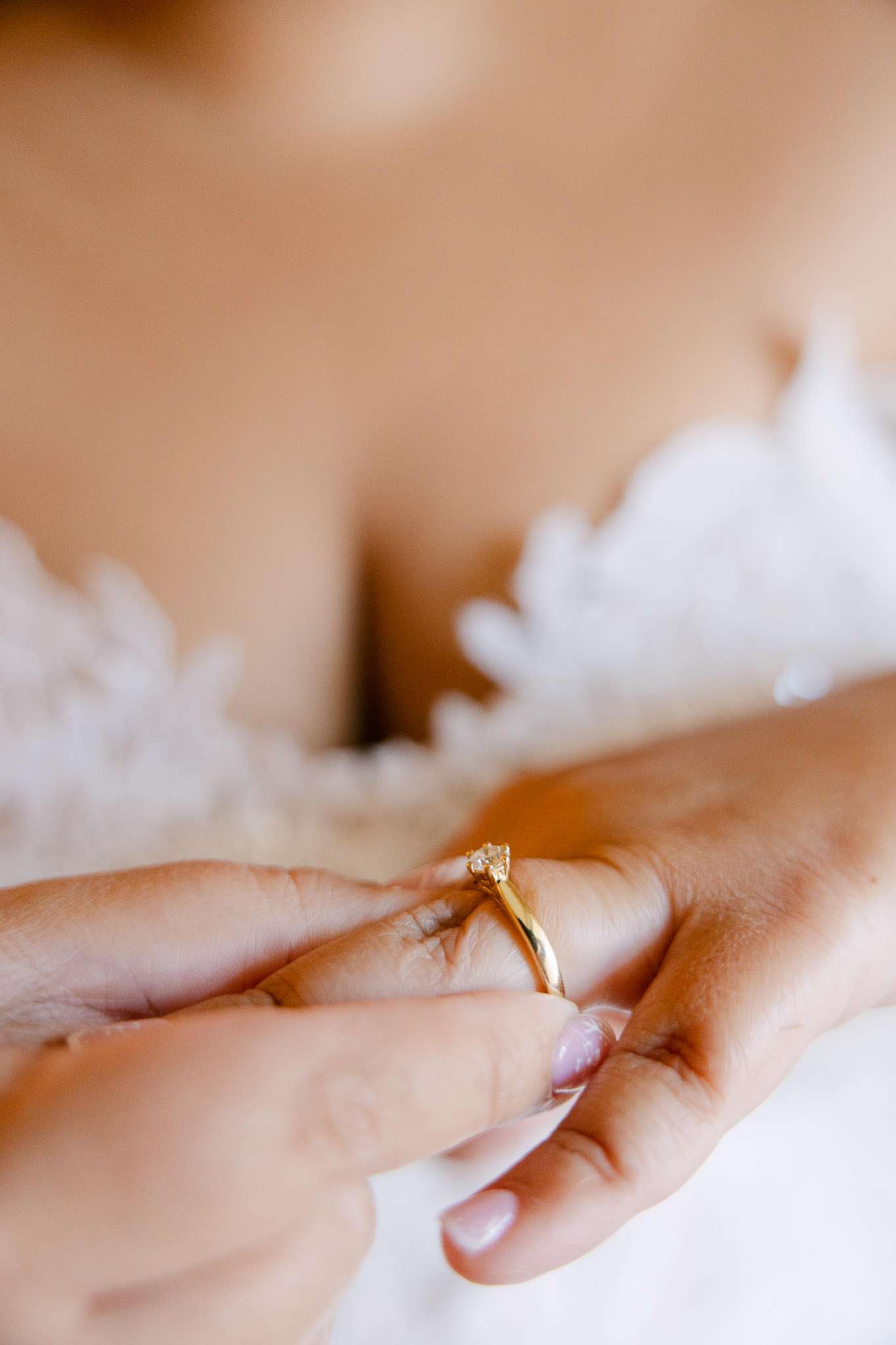 Close-up of bride holding gold solitaire diamond ring against lace wedding dress, editorial documentary wedding photography Portugal
