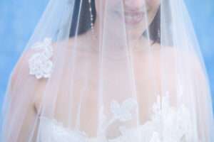 Bride smiling under sheer lace-trimmed veil, floral appliqué wedding dress, documentary wedding photography Ericeira Portugal