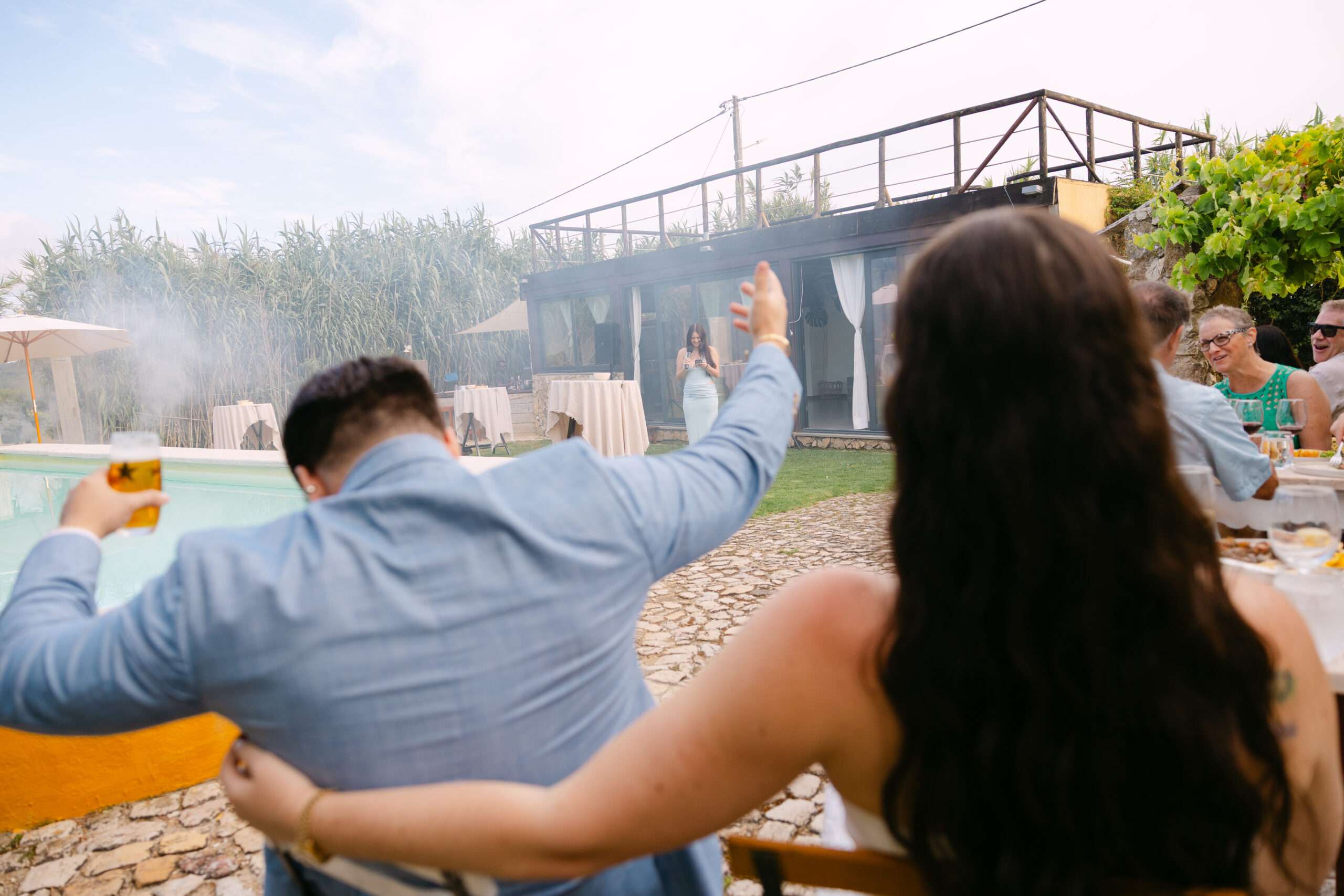 Wedding guests cheering and waving at outdoor poolside reception, Alma do Paço destination wedding Ericeira Portugal