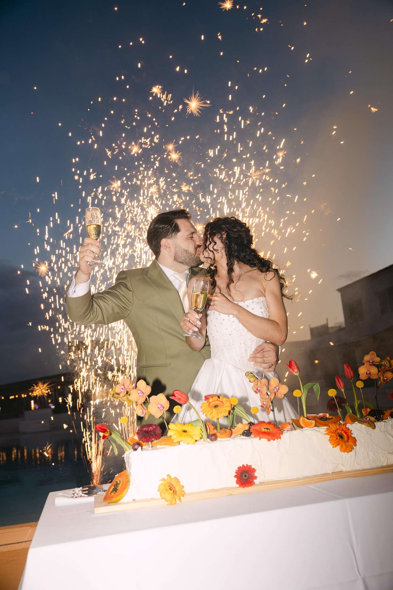 Couple kissing at wedding cake cutting with sparklers, outdoor evening reception, Lisbon wedding photographer