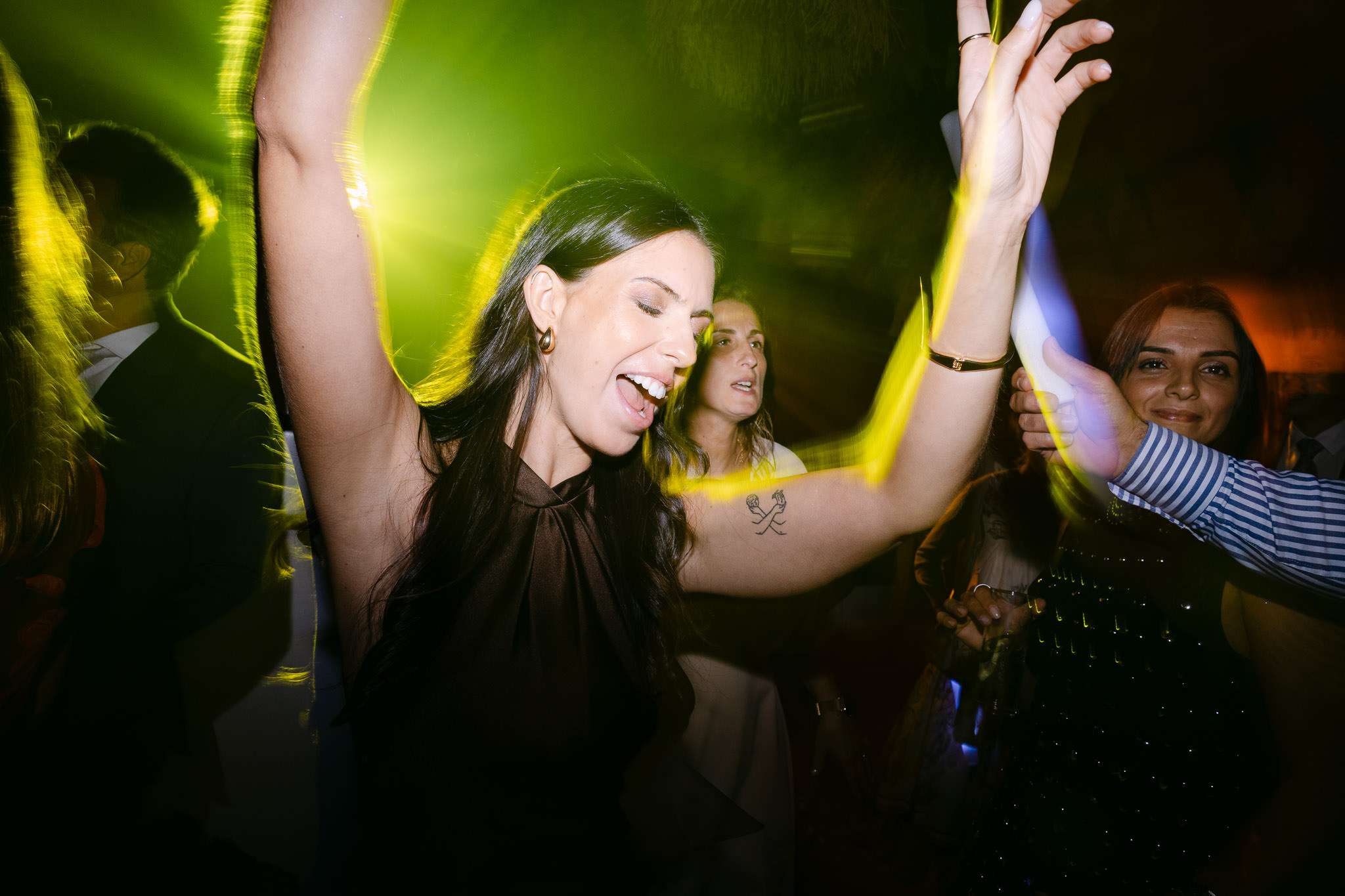 Guest dancing with arms raised under green lights, laughing with joy, candid reception moment, documentary wedding photography Lisbon