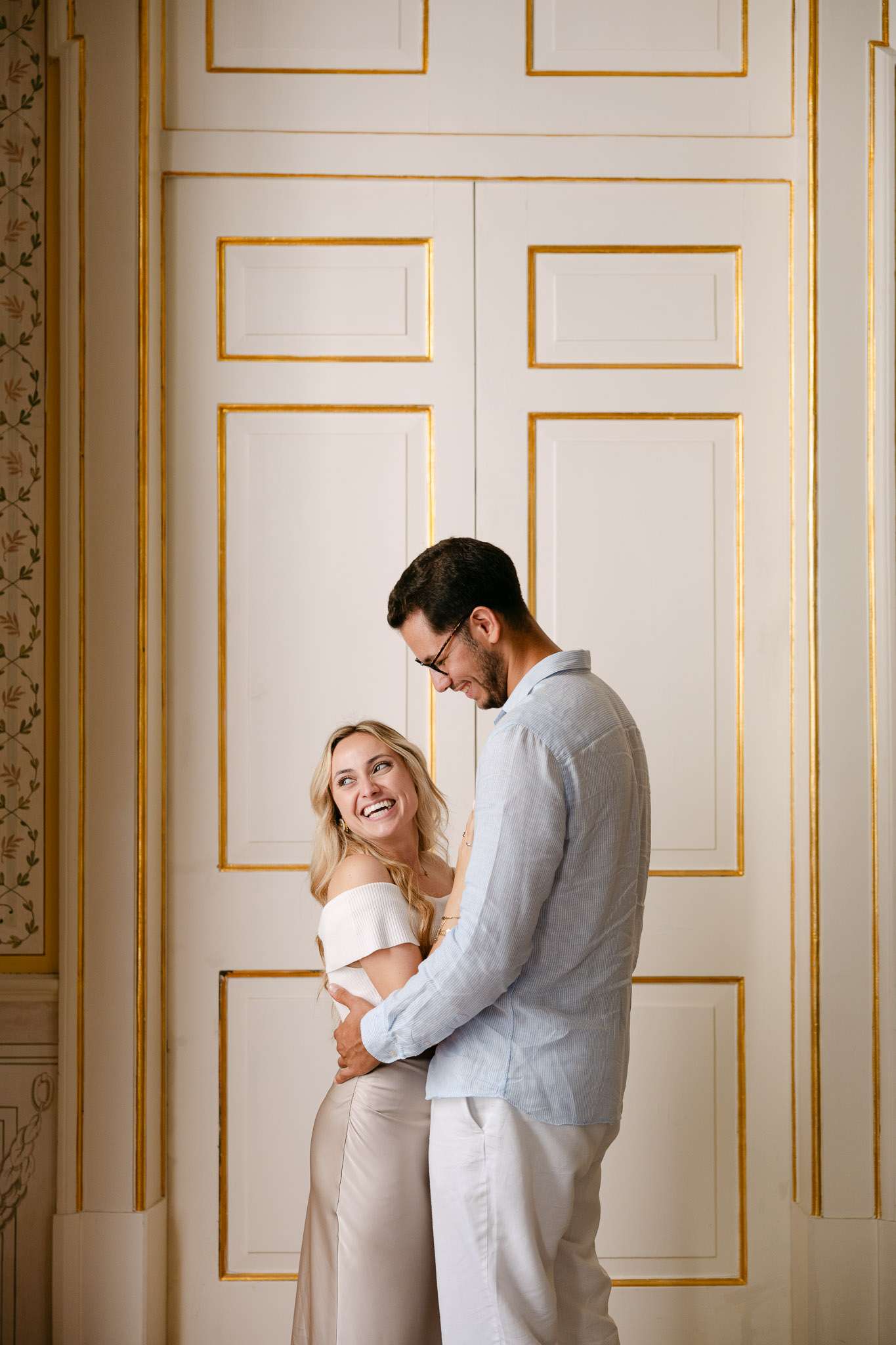 Newly engaged couple laughing together in front of ornate white and gold palace doors, Sintra, Portugal, candid proposal photography