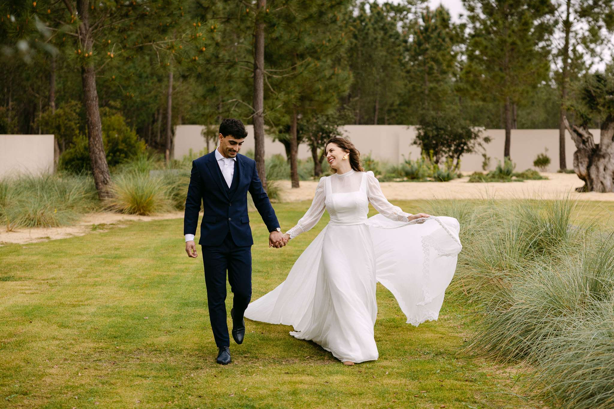 Comporta wedding photography of bride laughing with dress flowing as she walks hand in hand with groom on the lawn.