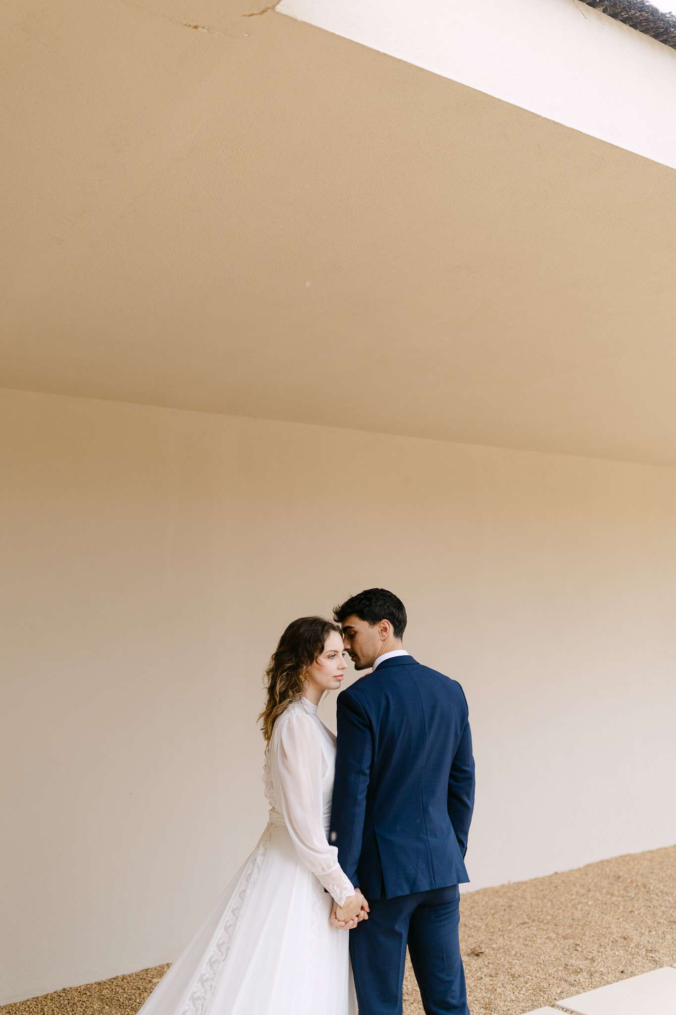 Comporta elopement photographer captures bride and groom in quiet embrace beneath modern architectural overhang.